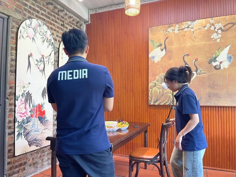 Nhân viên VNTAY mặc áo Media dàn dựng bàn chụp món trong phòng ăn treo tranh hạc Nhân viên VNTAY mặc áo Media dàn dựng bàn chụp món trong phòng ăn treo tranh hạc